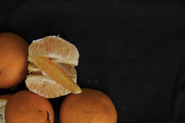 Soyulmuş portakal dilimlere bölünmüş kabuklu ryodm siyah bir arkaplanda yatıyor.