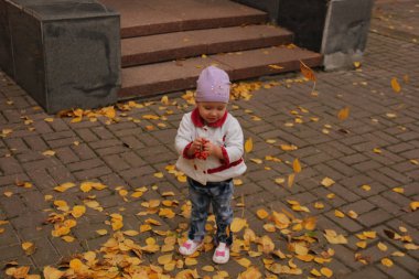 Çocuk, yukarıdan düşen sarı yaprakların üzerinde duruyor.