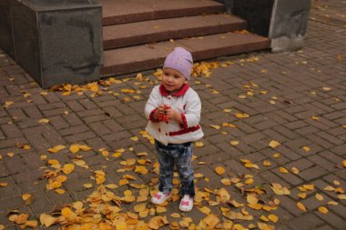 Çocuk, yukarıdan düşen sarı yaprakların üzerinde duruyor.