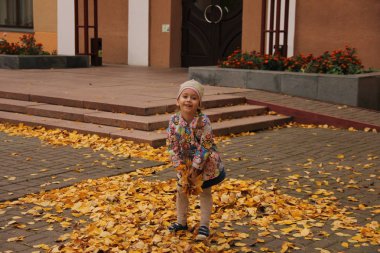 Sarı yaprakların üzerine atlayan parlak elbiseli bir kız. sonbahar eğlencesi