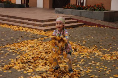 Sarı yaprakların üzerine atlayan parlak elbiseli bir kız. sonbahar eğlencesi