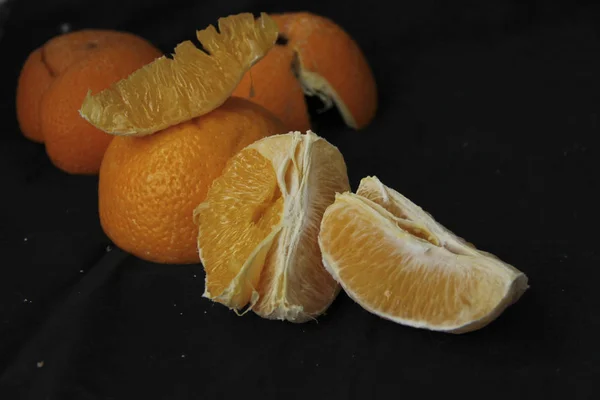 Naranja pelada dividida en rodajas ryodm con cáscara se encuentra sobre un fondo negro — Foto de Stock