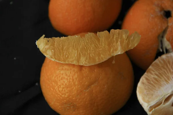 Geschälte Orange unterteilt in Scheiben mit Schale liegt auf schwarzem Hintergrund — Stockfoto