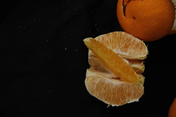 Geschälte Orange unterteilt in Scheiben mit Schale liegt auf schwarzem Hintergrund — Stockfoto