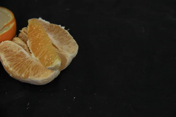 Naranja pelada dividida en rodajas ryodm con cáscara se encuentra sobre un fondo negro —  Fotos de Stock