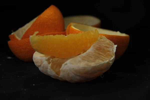 Laranja descascada dividida em fatias ryodm com casca encontra-se em um fundo preto — Fotografia de Stock