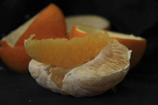 Очищений апельсин розділений на скибочки риодм з шкіркою лежить на чорному тлі — стокове фото