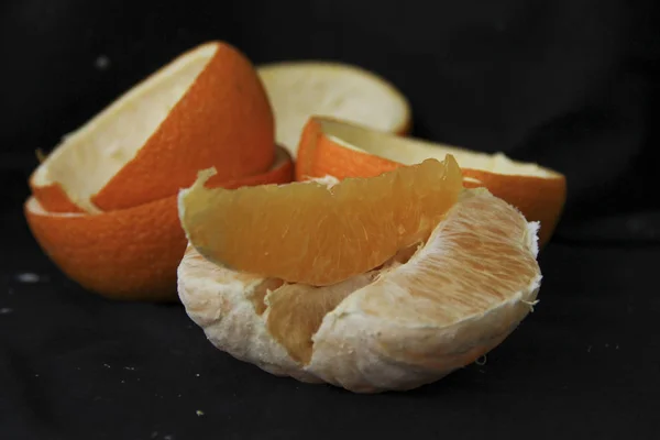 Очищенный апельсин, разделенный на ломтики риодм с кожурой лежит на черном фоне — стоковое фото