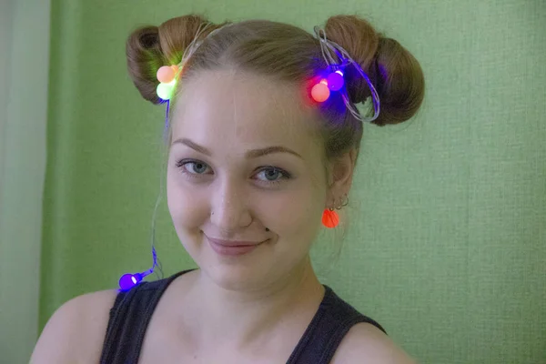 Stock image Pretty young blonde smiles with a magic sparkle in her hands, folded together. Garland is lit in different colors