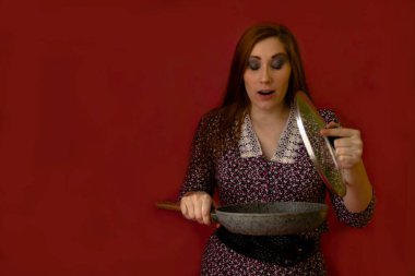 Genç ve seksi bir kadın kırmızı arka planda duruyor ve sürpriz bir şekilde tavanın kapağını kaldırıyor.