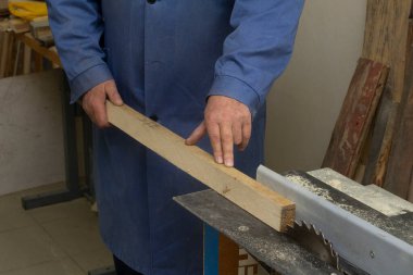 Yaşlı bir marangoz makinenin çubuğuyla ilgilenir. Erkekler araçlarla çalışır.