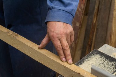 Yaşlı bir marangoz makinenin çubuğuyla ilgilenir. Erkekler araçlarla çalışır.