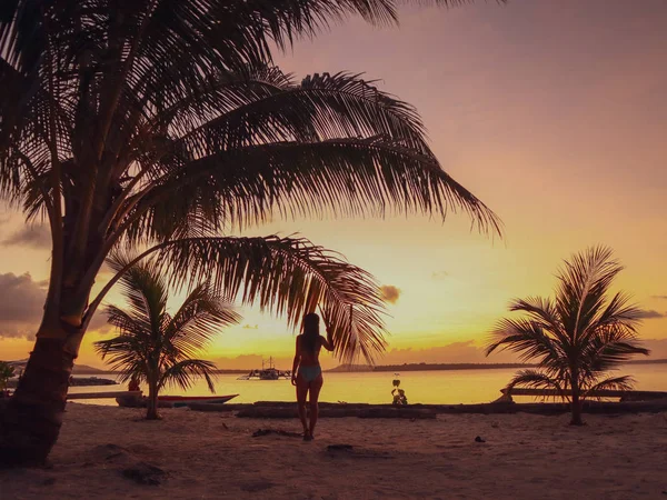 Woman watching sunset with palm trees in Candaraman Island in Balabac Philippines