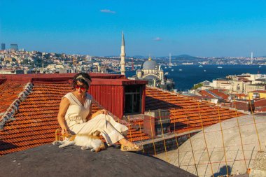 İstanbul'da boğaz arka planlı çatıda sarı kediye dokunan kadın