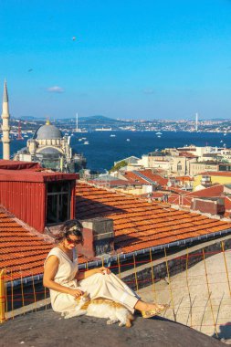 İstanbul'da boğaz arka planlı çatıda sarı kediye dokunan kadın