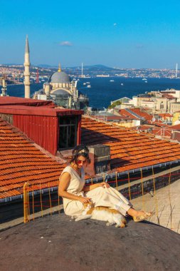 İstanbul'da boğaz arka planlı çatıda sarı kediye dokunan kadın