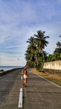 woman walking alone at the empty road with lots of palm trees in Cebu Island in Philippines clipart