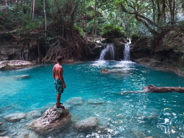 Cebu Adası'nda Kawasan Şelalesi turkuaz su ile şelale önünde bambu sal üzerinde tek başına fit adam, Filipinler