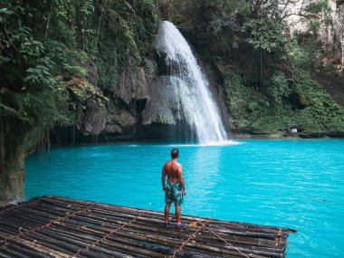 Cebu Adası'nda Kawasan Şelalesi turkuaz su ile şelale önünde bambu sal üzerinde tek başına fit adam, Filipinler