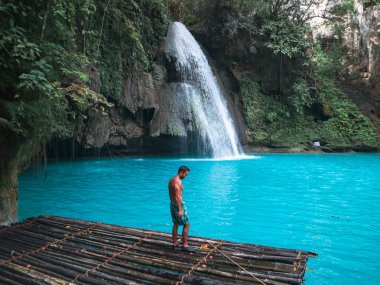 Cebu Adası'nda Kawasan Şelalesi turkuaz su ile şelale önünde bambu sal üzerinde tek başına fit adam, Filipinler