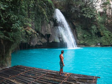 Cebu Adası'nda Kawasan Şelalesi turkuaz su ile şelale önünde bambu sal üzerinde tek başına fit adam, Filipinler