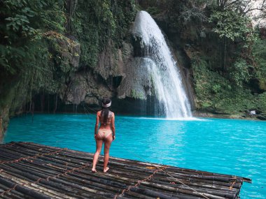 Cebu Adası'nda Kawasan Şelalesi turkuaz su ile şelale önünde bambu sal üzerinde fit kadın tek başına, Filipinler