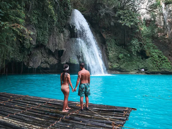 travel couple alone on the bamboo raft in front of the waterfall with turquoise water in Kawasan Falls in Cebu Island, Philippines