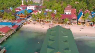 Kamboçya Koh Rong Adası'nda iskele yakınında turkuaz okyanus ve Uzun Kuyruk Tekneler yakın beyaz plaj ve palmiye ağacı manzara renkli evler ile Koh Touch köyünün havadan üst görünümü