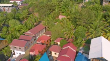 Kamboçya Koh Rong Adası'nda iskele yakınında turkuaz okyanus ve Uzun Kuyruk Tekneler yakın beyaz plaj ve palmiye ağacı manzara renkli evler ile Koh Touch köyünün havadan üst görünümü