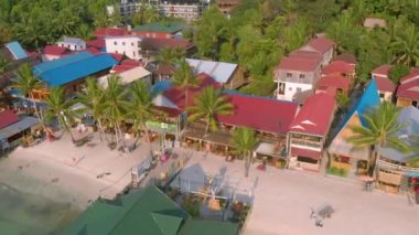 Kamboçya Koh Rong Adası'nda iskele yakınında turkuaz okyanus ve Uzun Kuyruk Tekneler yakın beyaz plaj ve palmiye ağacı manzara renkli evler ile Koh Touch köyünün havadan üst görünümü