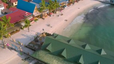 Kamboçya Koh Rong Adası'nda iskele yakınında turkuaz okyanus ve Uzun Kuyruk Tekneler yakın beyaz plaj ve palmiye ağacı manzara renkli evler ile Koh Touch köyünün havadan üst görünümü