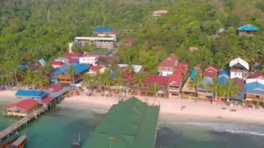 Kamboçya Koh Rong Adası'nda iskele yakınında turkuaz okyanus ve Uzun Kuyruk Tekneler yakın beyaz plaj ve palmiye ağacı manzara renkli evler ile Koh Touch köyünün havadan üst görünümü