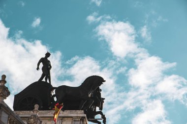 Madrid 'de açık mavi gökyüzünde bir binanın çatısındaki Quadriga heykeli.