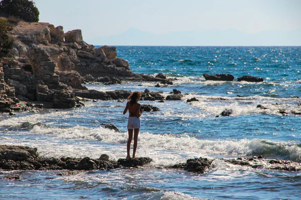 Woman alone at the rocky beach looking over the horizon with  wavy sea on a wind day in Mediterranean