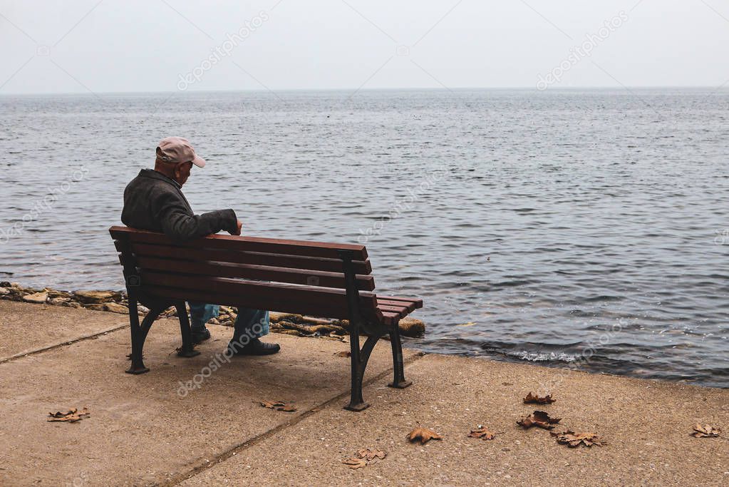 old man sitting at the bench looking to the horizon over the sea