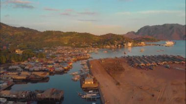 Palawan, Filipinler 'deki Busuanga Adası' nda bekleyen deniz limanı ve turist botlarıyla Coron kasabasının hava manzarası. Gün batımında dağ ve kasaba manzarası