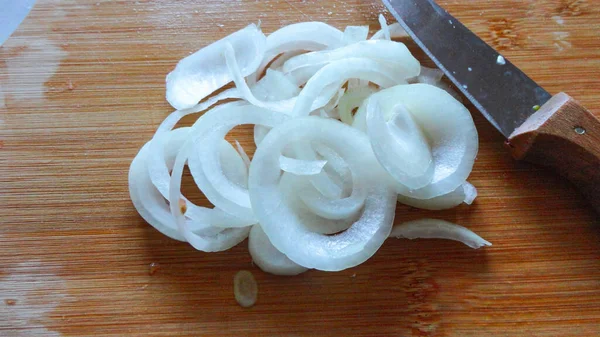 Raw sliced white onion on wooden chopping board ready to cook