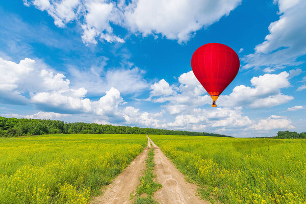 Red hot air balloon above the dirty road on the meadow.