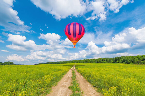 Red hot air balloon above the dirty road on the meadow.