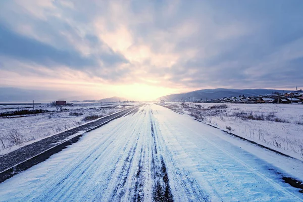 Highway to the small settlement at cold winter sunset time.