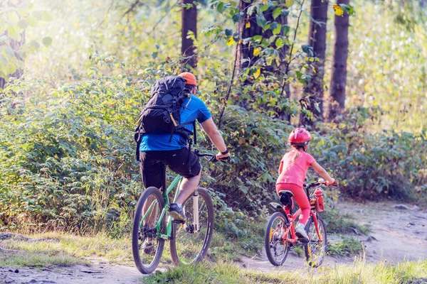 Father and daughter ride the bicycles on the forest path.
