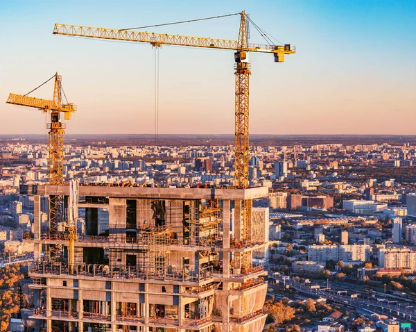 Cranes above the skyscraper construction site at sunset time.