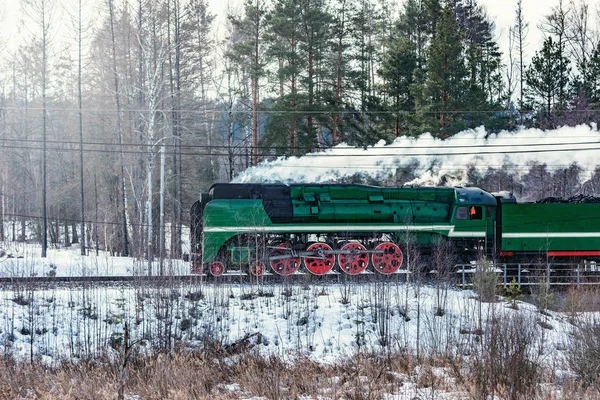Steam train moves forward at cold winter morning time.
