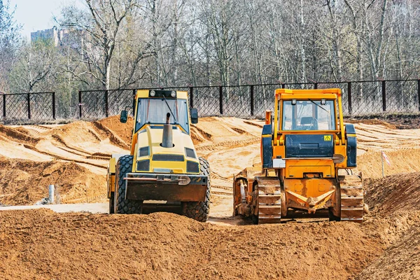 Bulldozer and road roller stand on the construction site.
