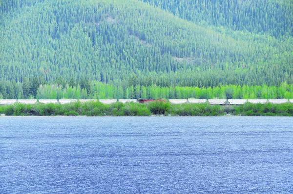Lungo treno merci si muove vicino al lago nelle Montagne Rocciose canadesi . — Foto Stock