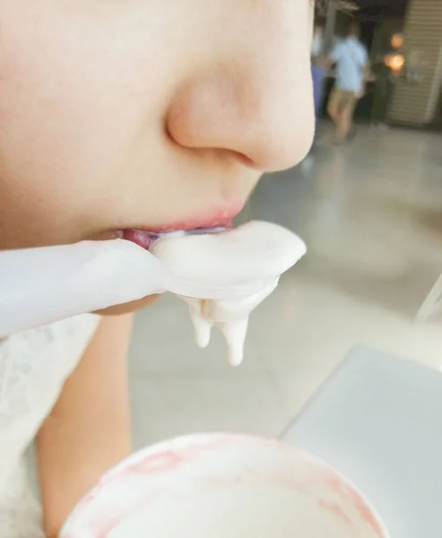 Cute girl eating ice cream in a cafe. A drop of ice cream is dripping from a spoon.