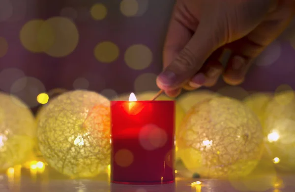 Frohe Weihnachten und ein gutes neues Jahr, Grußkarte. Hand, die eine Kerze entzündet.Schöne Dekoration für die Feiertage. Hand, die eine Kerze anzündet. dekorativer roter Hintergrund und goldener Bokeh-Kranz. chris — Stockfoto