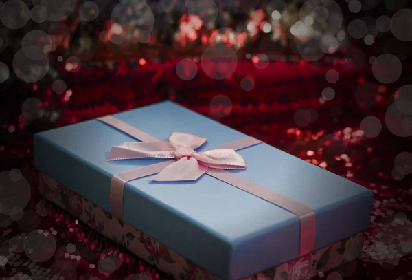 Cadeaudoosjes liggen op een rood glanzende stof. Pakket van geschenken voor Christmas.bokeh, kleine boom, heldere feestelijke achtergrond. Vignette Kerst geschenken.Kerst cadeau.Kerst winkelen. — Stockfoto