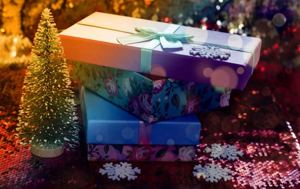 Cadeaudoosjes liggen op een rood glanzende stof. Pakket van geschenken voor Christmas.bokeh, kleine boom, heldere feestelijke achtergrond. Kerstcadeau.Kerstcadeau.Kerstinkopen. — Stockfoto