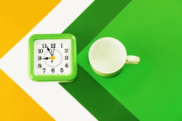 Time management.Koncept pracovní doby, pracovní den. Čas na práci. Barvy: zelená, tmavě zelená, žlutá, oranžová. Na vícebarevném pozadí, bílý prázdný šálek kávy nebo čaje. Vedle ní je wa. — Stock fotografie